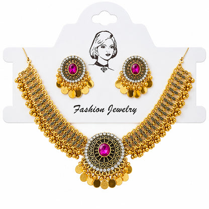 Gold-toned traditional jewelry set with a statement necklace and matching earrings, featuring bright pink gemstones and dangling gold coins, displayed on a white card over a satin fabric background.