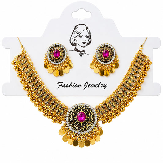 Gold-toned traditional jewelry set with a statement necklace and matching earrings, featuring bright pink gemstones and dangling gold coins, displayed on a white card over a satin fabric background.